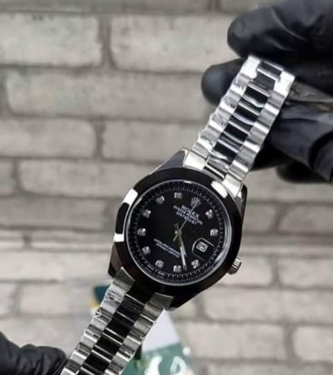 Rolex Datejust style watch featuring a black dial with stone markers and a stainless steel bracelet.